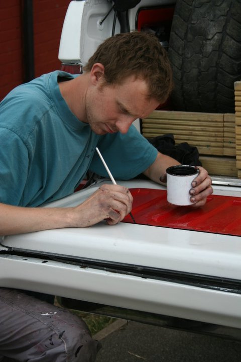 1989 Ford Bronco - Detailing work in progress: a man applies a red stripe to a white surface.