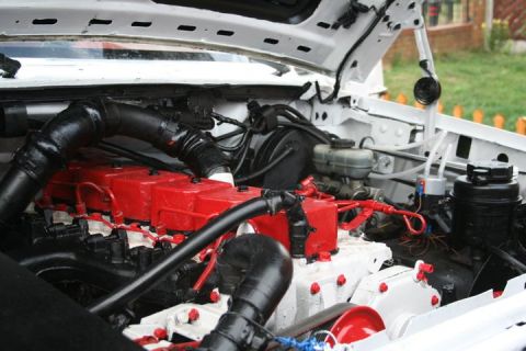 1989 Ford Bronco - Close-up view of a white vehicle's engine bay, showing a red engine block and various hoses.