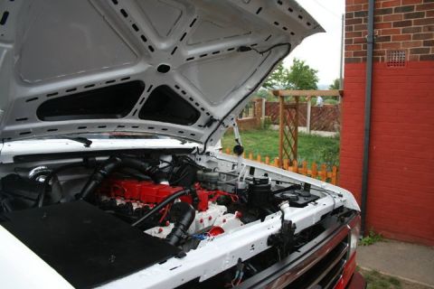 1989 Ford Bronco - The engine bay of a white 1989 Ford Bronco, a prominent red engine block and "SUPERMOTORS" branding.