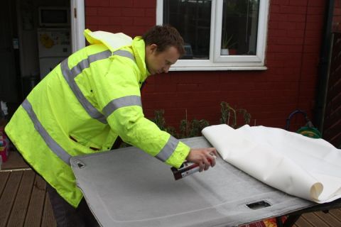 1989 Ford Bronco - A person sprays adhesive onto a car headliner, preparing it for reupholstering.