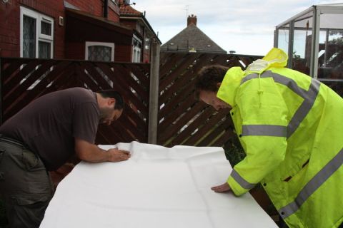 1989 Ford Bronco - Two men are examining a large white tarp spread out on a surface. A Supermotors.net logo is visible in the lower right corner.