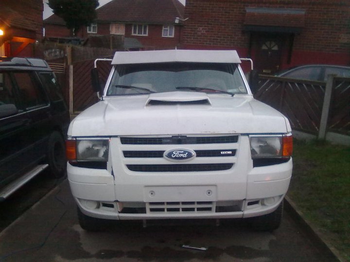 White Ford pickup truck with a hood scoop and a visor, front view. Damage to the front bumper