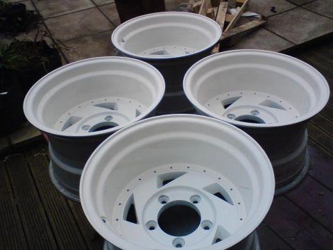 1989 Ford Bronco - Four white rims are shown stacked on a wooden deck, possibly after being painted.