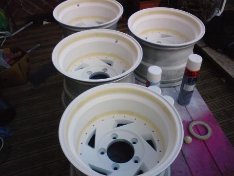 1989 Ford Bronco - Four white rims are laid out on a wooden deck, ready for painting, with spray cans nearby.
