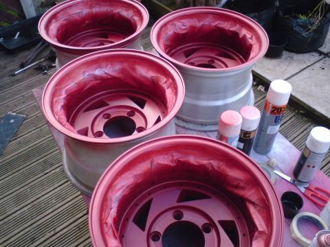 1989 Ford Bronco - Four rims are shown after being painted red, with spray cans and tape nearby on a wooden deck.