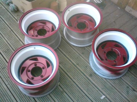 1989 Ford Bronco - A set of four custom alloy wheels, red centers and white rims, are displayed on a wooden surface.