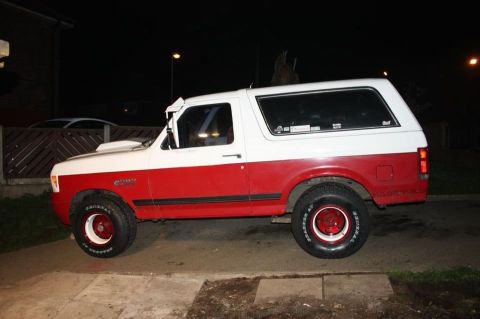 1989 Ford Bronco - This two-tone red and white 1989 Ford Bronco is seen from the side, aftermarket wheels and a hood scoop.