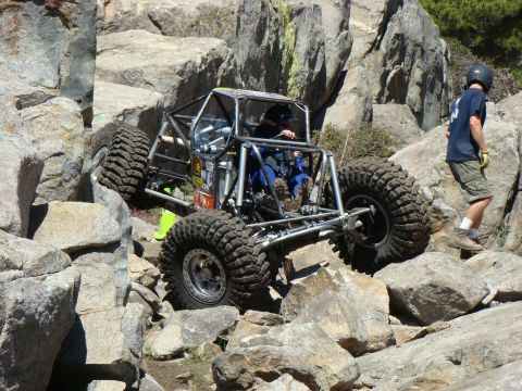 1989 Ford Bronco - A custom off-road buggy tackles a challenging rocky incline with a spotter on the side.