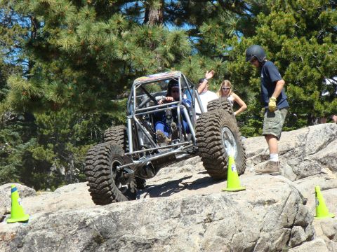 1989 Ford Bronco - A custom-built off-road buggy with a prominent roll cage tackles a challenging rocky course, with spectators observing.