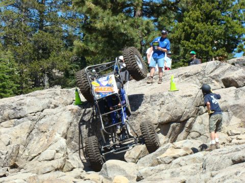 1989 Ford Bronco - An off-road buggy navigates a steep, rocky course with spectators observing the challenging terrain.