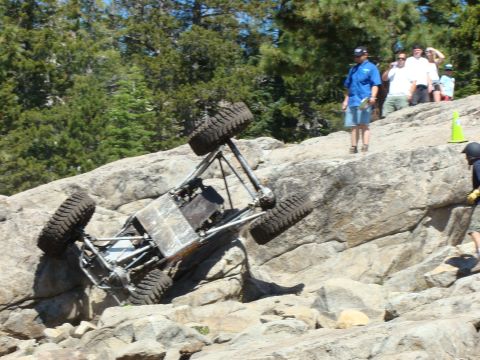 1989 Ford Bronco - An off-road buggy is stuck on a steep, rocky incline during an event, with onlookers observing the situation.