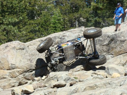 1989 Ford Bronco - An off-road buggy is overturned on a rocky incline, with spectators observing.