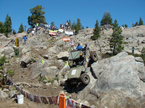 1989 Ford Bronco - An off-road vehicle navigates a challenging rocky terrain during a competition, with spectators watching from the hillside.