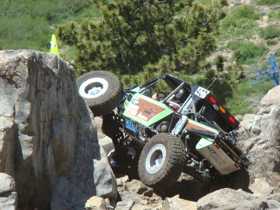 Off-road buggy with number 407 on it is climbing over large rocks on a trail