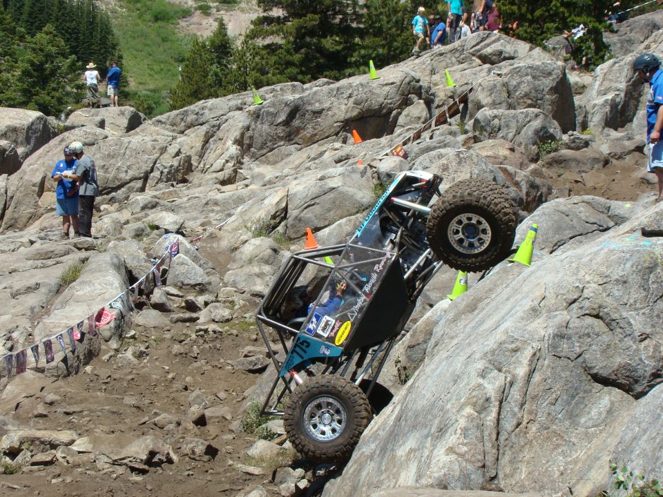 Off-road buggy climbing a steep, rocky incline with large tires and a roll cage