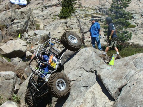 1989 Ford Bronco - A heavily modified off-road buggy navigates a treacherous rocky terrain with spectators observing the difficult climb.