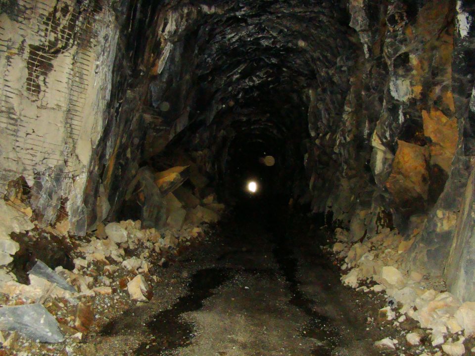 Dark, rough-hewn mine tunnel with debris on the floor and walls