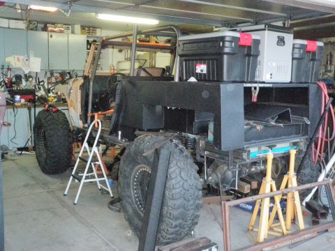 1961 International Scout 800 - A custom off-road vehicle is in a garage, undergoing modifications with large tires and a roll cage structure visible.