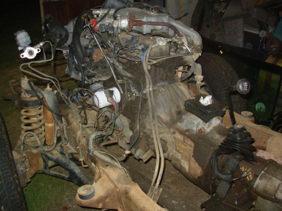 Dusty engine and manual transmission assembly with shifter removed from a truck, on a shop floor.