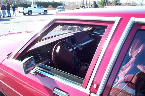 1991 Ford LTD Crown Victoria - Interior view of a red car, showing the dashboard, steering wheel, and seats. Other vehicles are visible in the background.