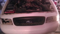 2004 Ford Crown Victoria - Front view of a white Ford Crown Victoria with its hood open, revealing the engine.