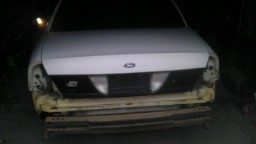 2004 Ford Crown Victoria - The front end of a white vehicle is visible, showing a black grille and damage to the bumper and headlight areas.