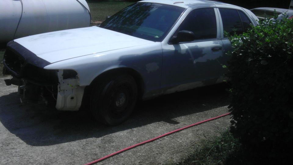 2004 Ford Crown Victoria with front end damage, primer on body panels, parked outside