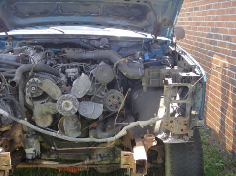 1994 Ford Bronco - The engine compartment of a disassembled blue truck is shown with the hood open, revealing the engine and surrounding parts.