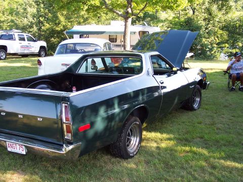 1975 Ford Ranchero - A dark green Ford Ranchero is parked on grass with its hood open, while other vehicles and a camper are visible in the background.