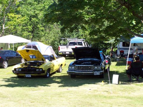 1975 Ford Ranchero - A yellow 1975 Ford Ranchero with a tent on its bed is displayed next to a black car at an outdoor event.