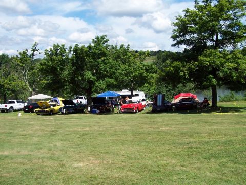 1975 Ford Ranchero - Several vehicles and tents are set up on a grassy field under a partly cloudy sky.
