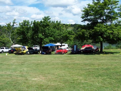 1975 Ford Ranchero - A gathering of vehicles, RVs, and tents are set up on a grassy field under a cloudy sky.