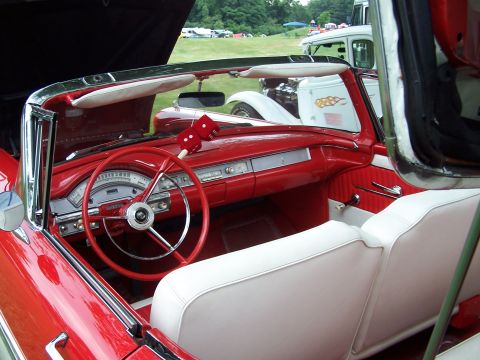 1975 Ford Ranchero - The interior of a red and white convertible shows a classic dashboard and steering wheel, with other vehicles visible in the background.