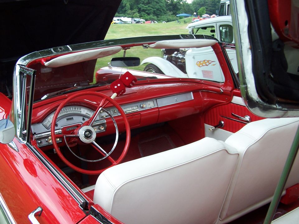 Red 1950s Ford convertible interior with white bench seat, red steering wheel and fuzzy dice