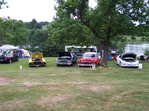 1975 Ford Ranchero - A car show scene with multiple vehicles displayed on a grassy field next to a lake.