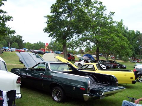 1975 Ford Ranchero - Several vehicles are parked on a grassy field under trees, with tents and other cars in the background.