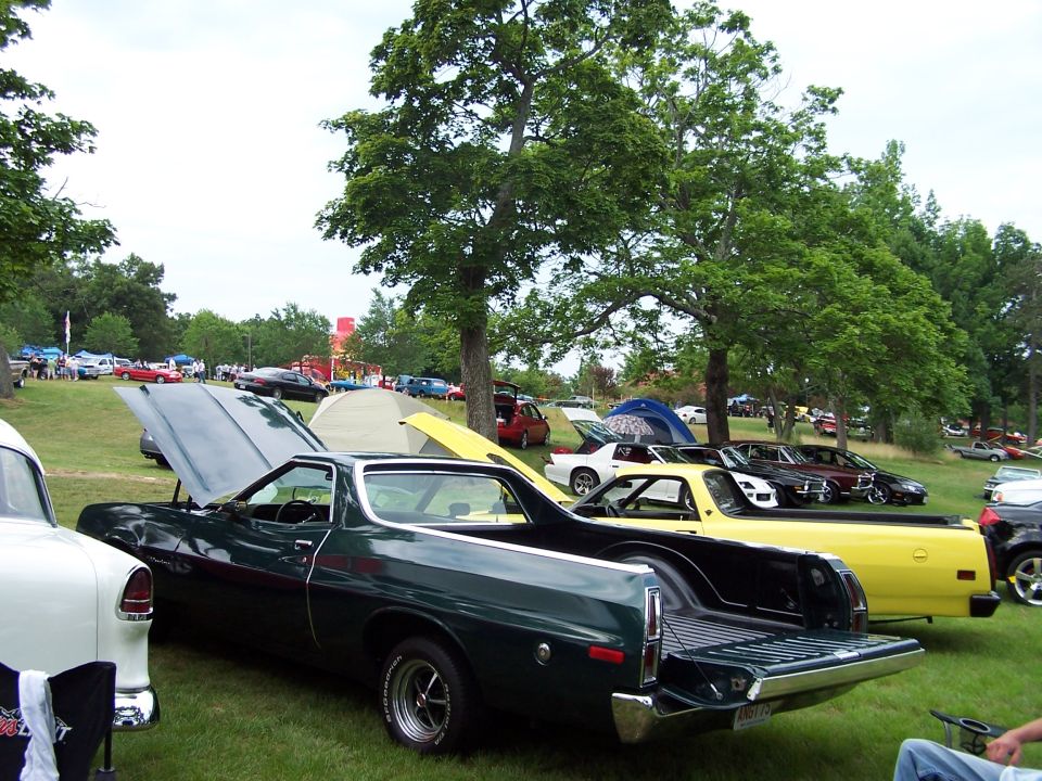 Dark green 1970s Ford Ranchero with hood up at a grassy car show, rear three-quarter view