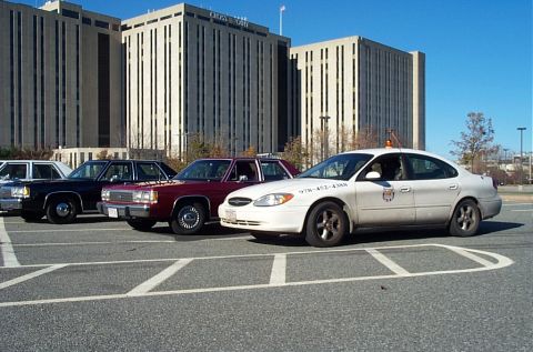 1991 Ford LTD Crown Victoria - A maroon Ford Crown Victoria sedan is parked in a lot with other vehicles, with a large building in the background.