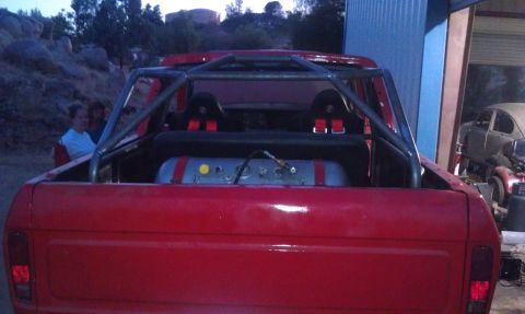 1978 Ford Bronco - The rear of a red pickup truck is shown with a custom roll cage and racing seats installed.
