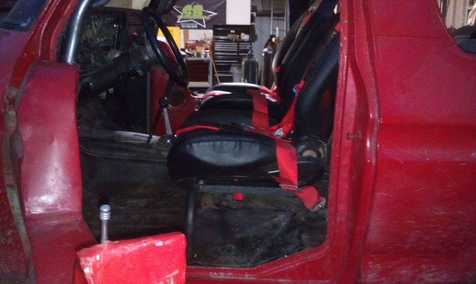 Red interior with racing seats, red harnesses, and roll cage visible