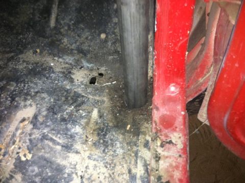 1978 Ford Bronco - The interior of a vehicle shows a roll cage tube and red body paneling with some dirt and rust.