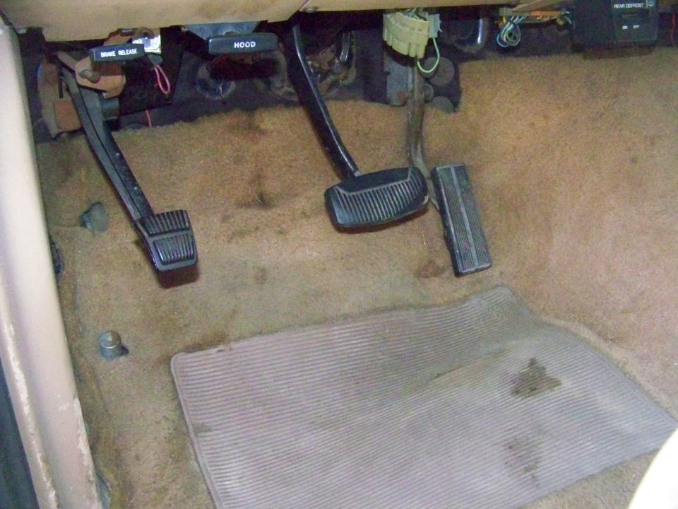 1985 Ford Bronco interior footwell with brake, clutch, and accelerator pedals, and a floor mat