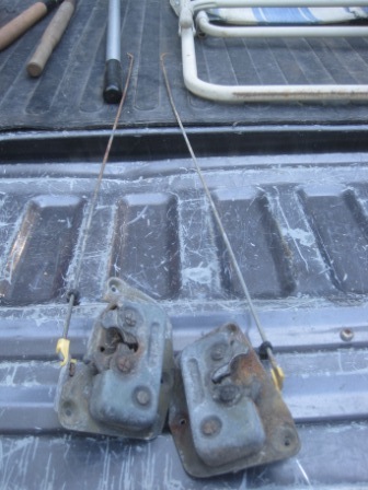 1993 Ford Bronco - Two door latches and their associated rods are shown resting on a truck bed, likely for parts.