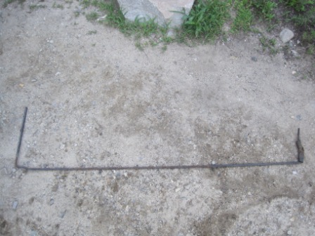 1993 Ford Bronco - A metal rod is shown lying on a gravelly surface with some grass and rocks in the background.