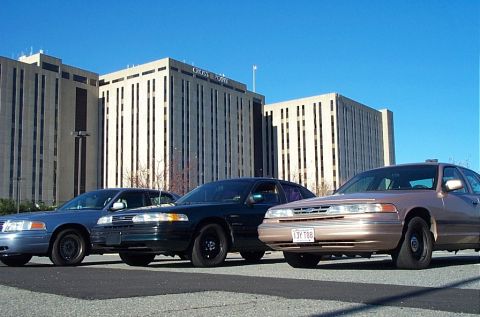 1991 Ford LTD Crown Victoria - Three Ford Crown Victorias, likely from the mid-1990s, are parked in front of a large office building.