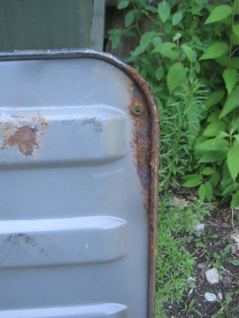 1993 Ford Bronco - Close-up of a rusted metal part, possibly from a vehicle, with green foliage in the background.