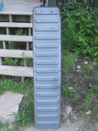 1993 Ford Bronco - A gray tailgate panel with a ribbed surface is shown outdoors, leaning against a wooden structure.