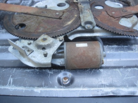 1993 Ford Bronco - A close-up view of a rusty window regulator mechanism, including the motor and gears.