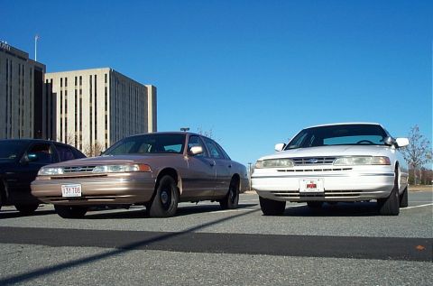 1991 Ford LTD Crown Victoria - Two Ford Crown Victoria police cars are parked side-by-side under a clear blue sky.