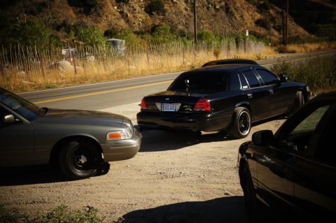 2003 Ford Crown Victoria - Lowered black Crown Victoria on a dirt pullout flanked by a gray sedan along a canyon road.